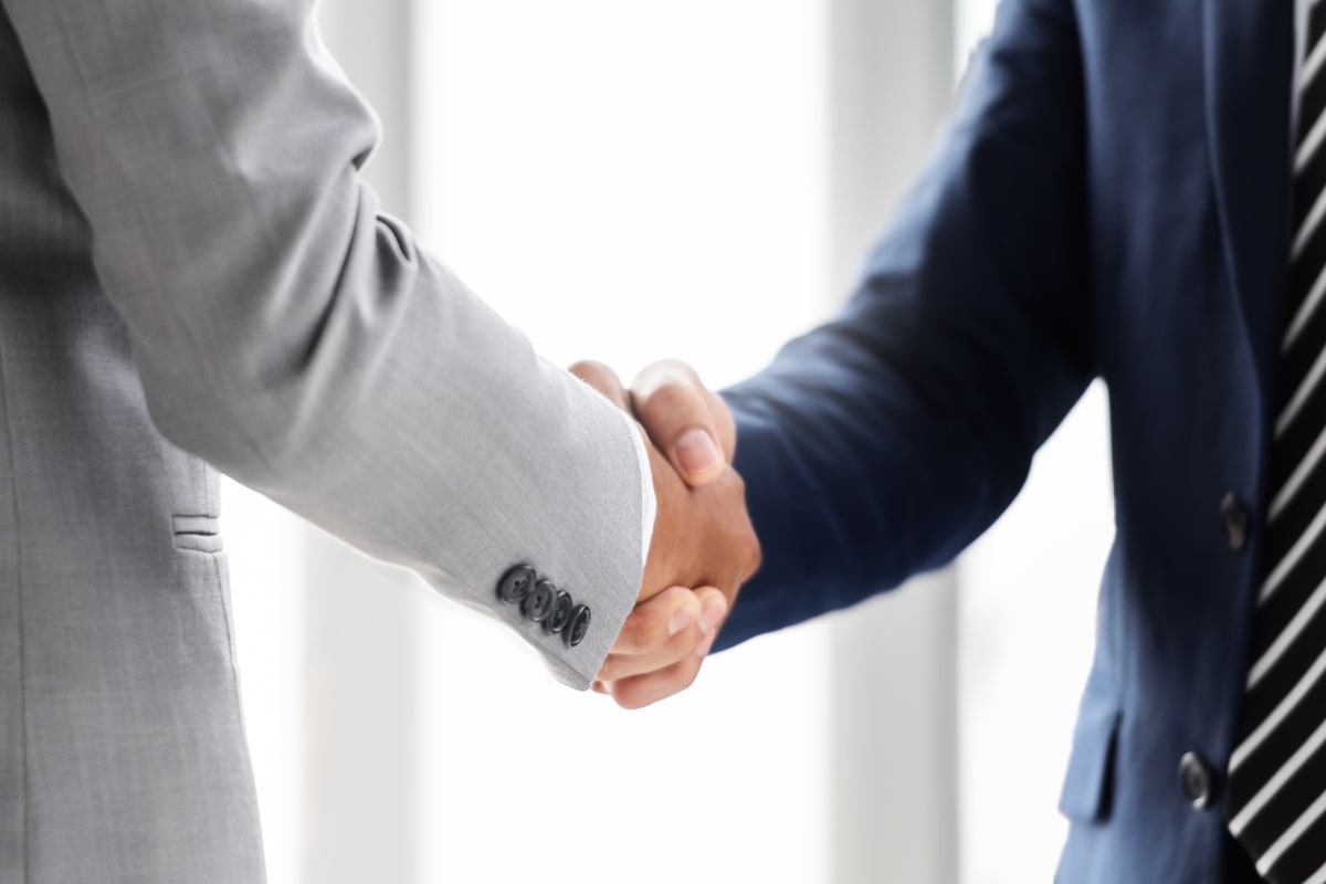 Two businessmen, one in gray suit, one in blue suit with stripe tie, shaking hands