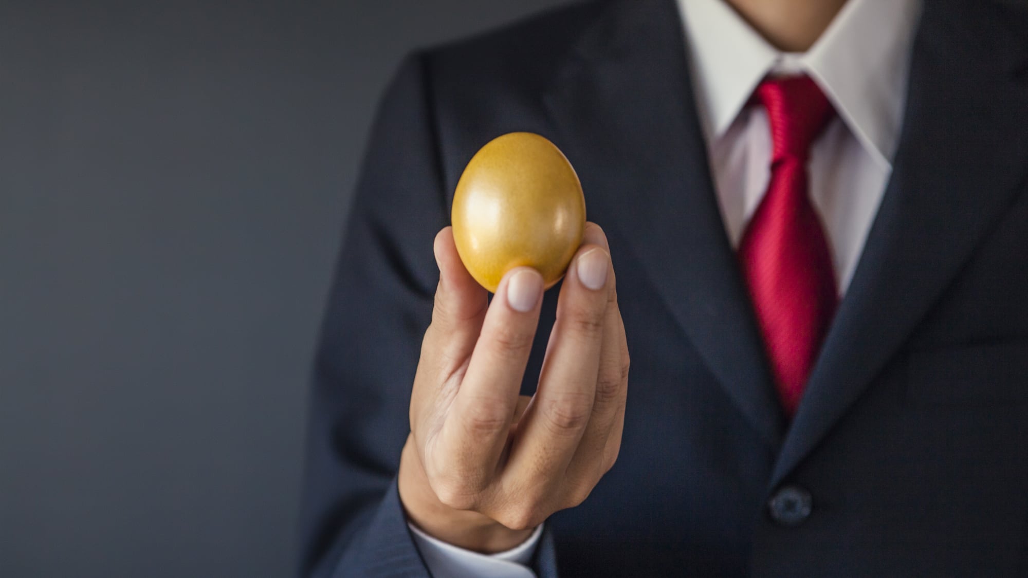 man in a suit with red tie holding a golden egg