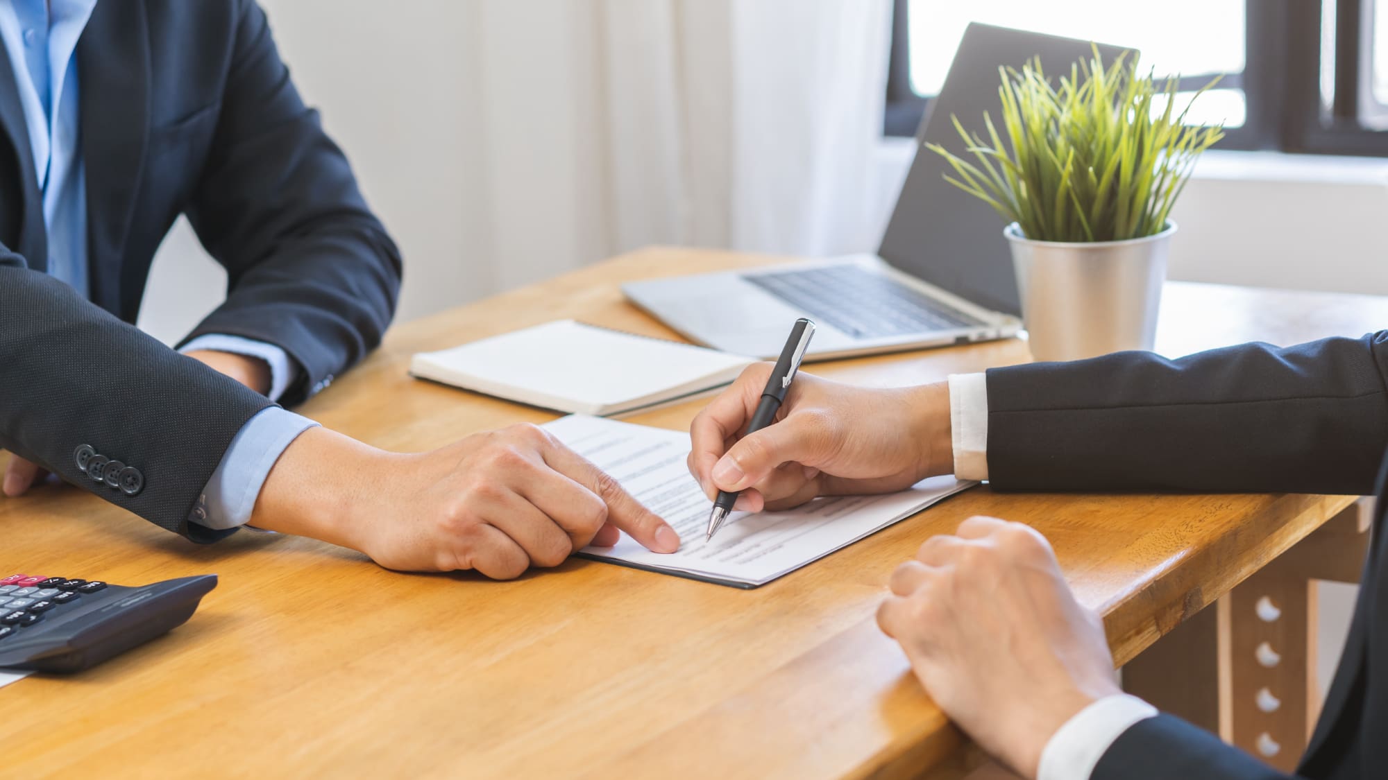business people sitting at a wooden desk signing a contract